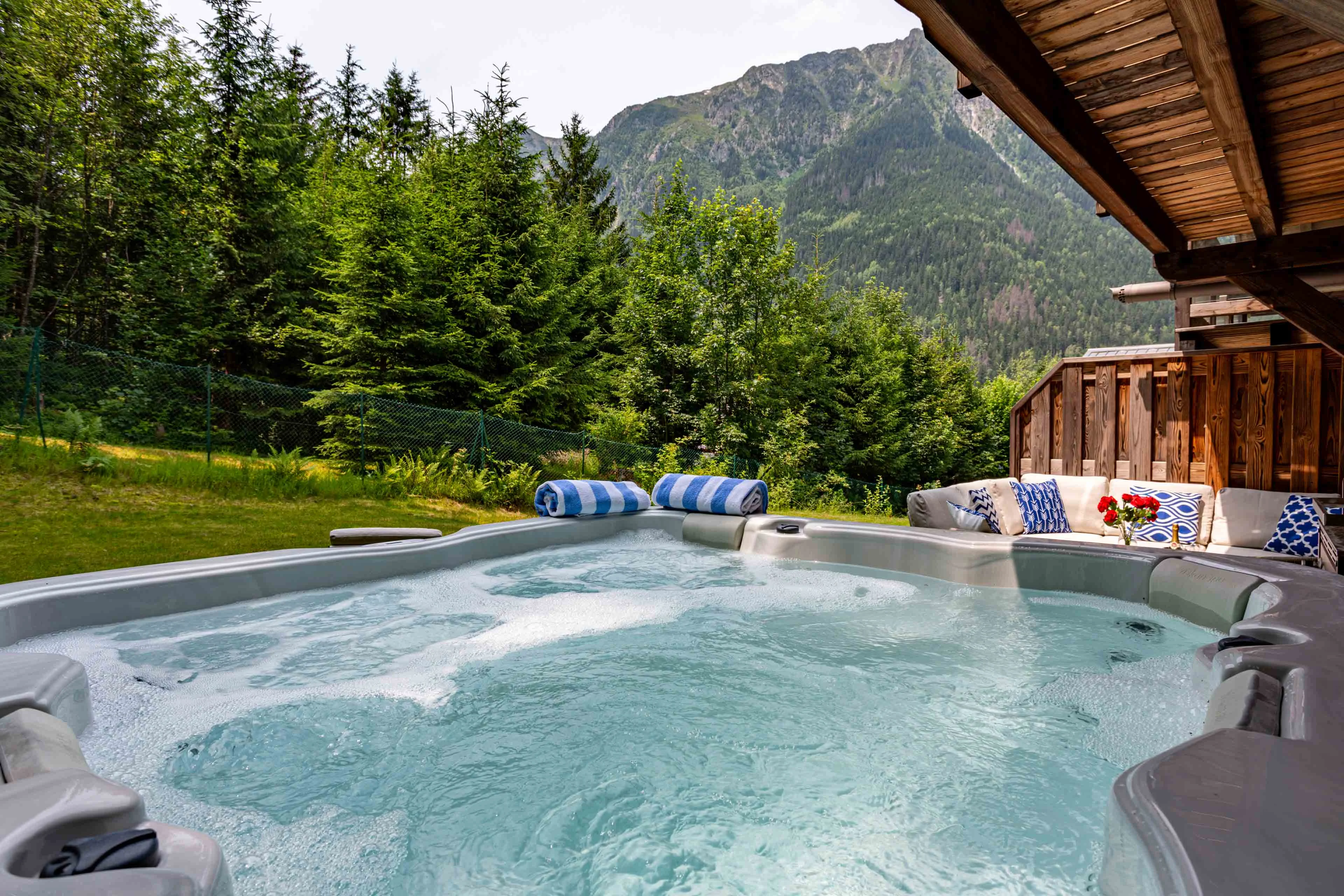 Bain à remous extérieur sous l'auvent d'un chalet à Chamonix, entouré de sapins avec une crête de montagne en arrière plan