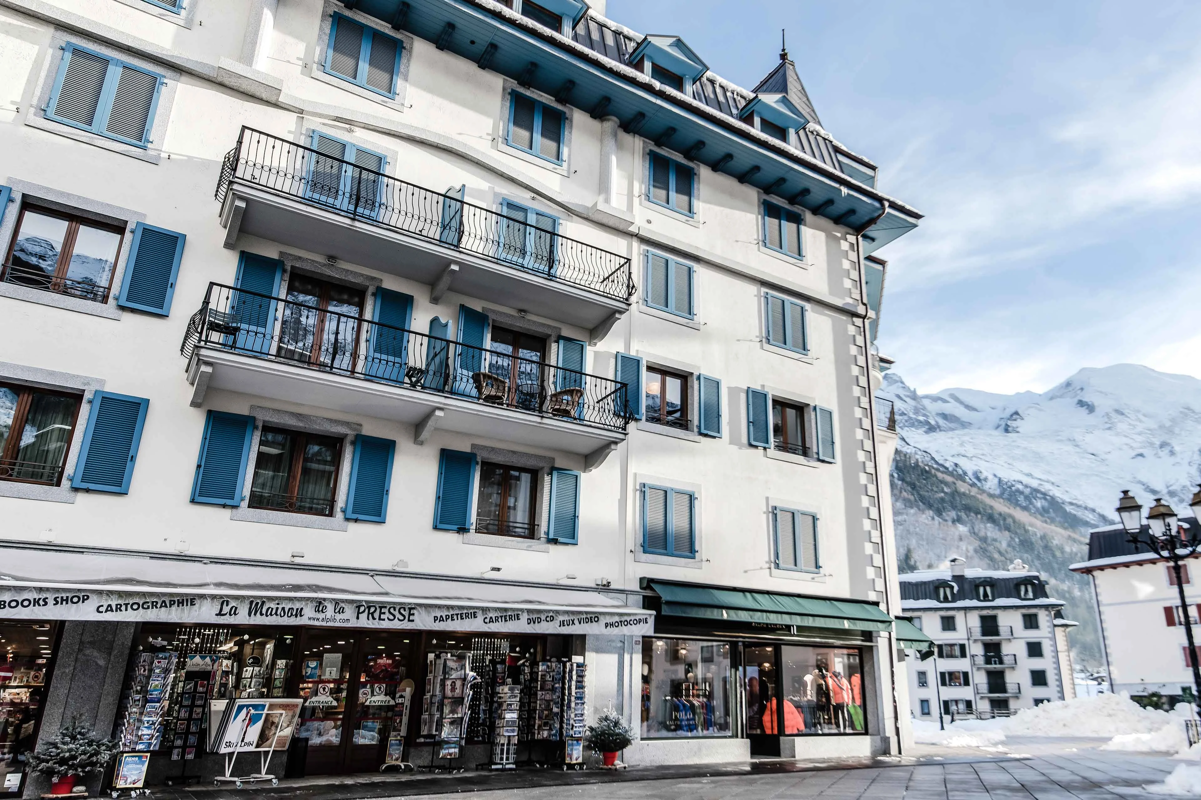 Immeuble aux volets bleus au-dessus des commerces au centre de Chamonix, avec les montagnes enneigées en arrière plan