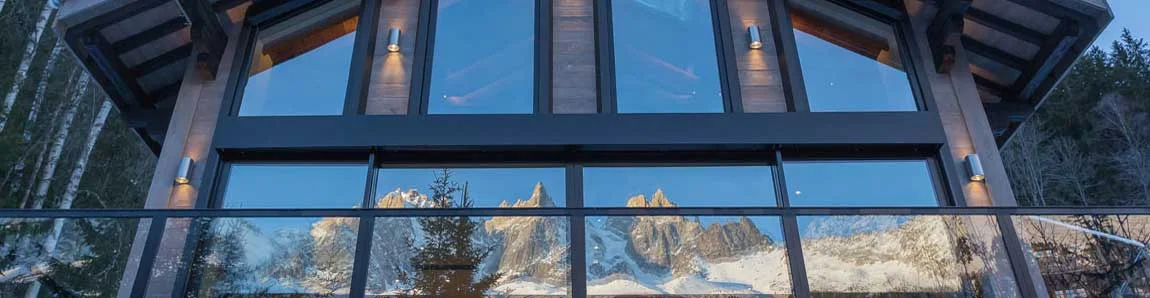 Baies vitrées d'un chalet à Chamonix reflétant les Aiguilles enneigées au crépuscule