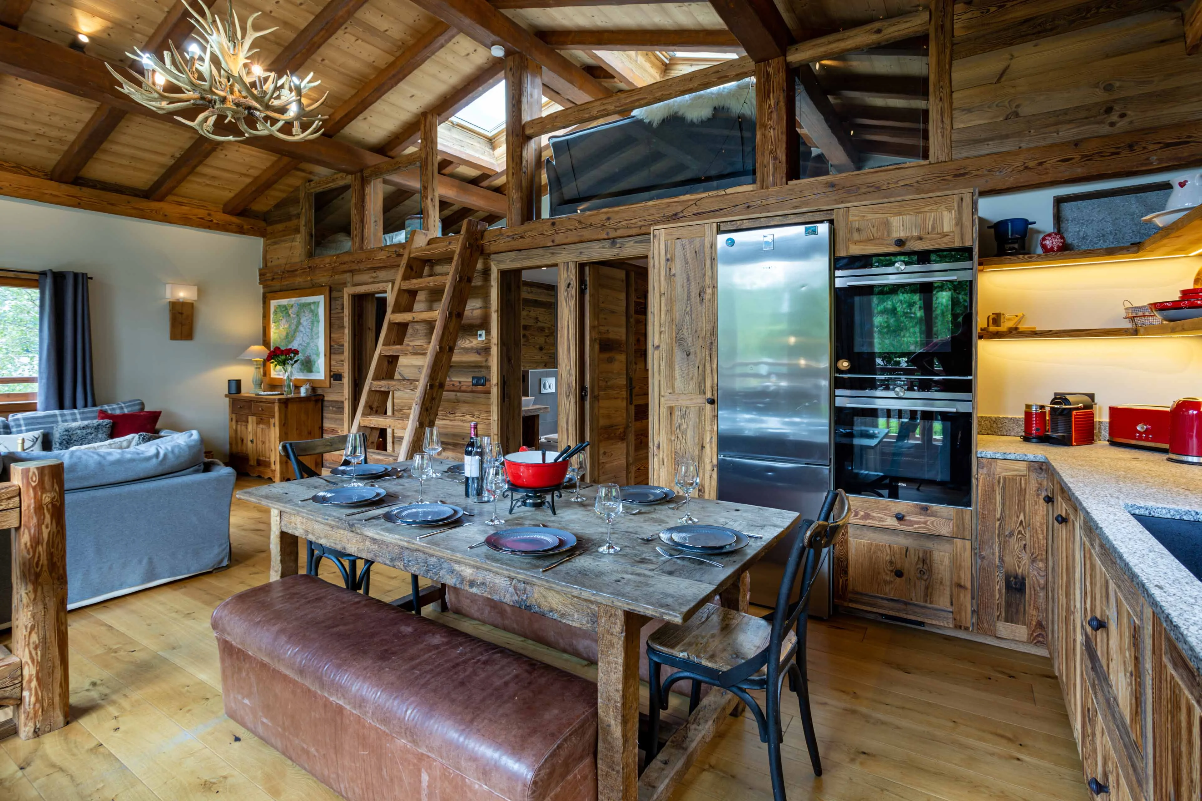 Cuisine et salle à manger ouvertes dans un chalet à Chamonix, avec bois ancien, échelle de mezzanine et table dressée pour une fondue