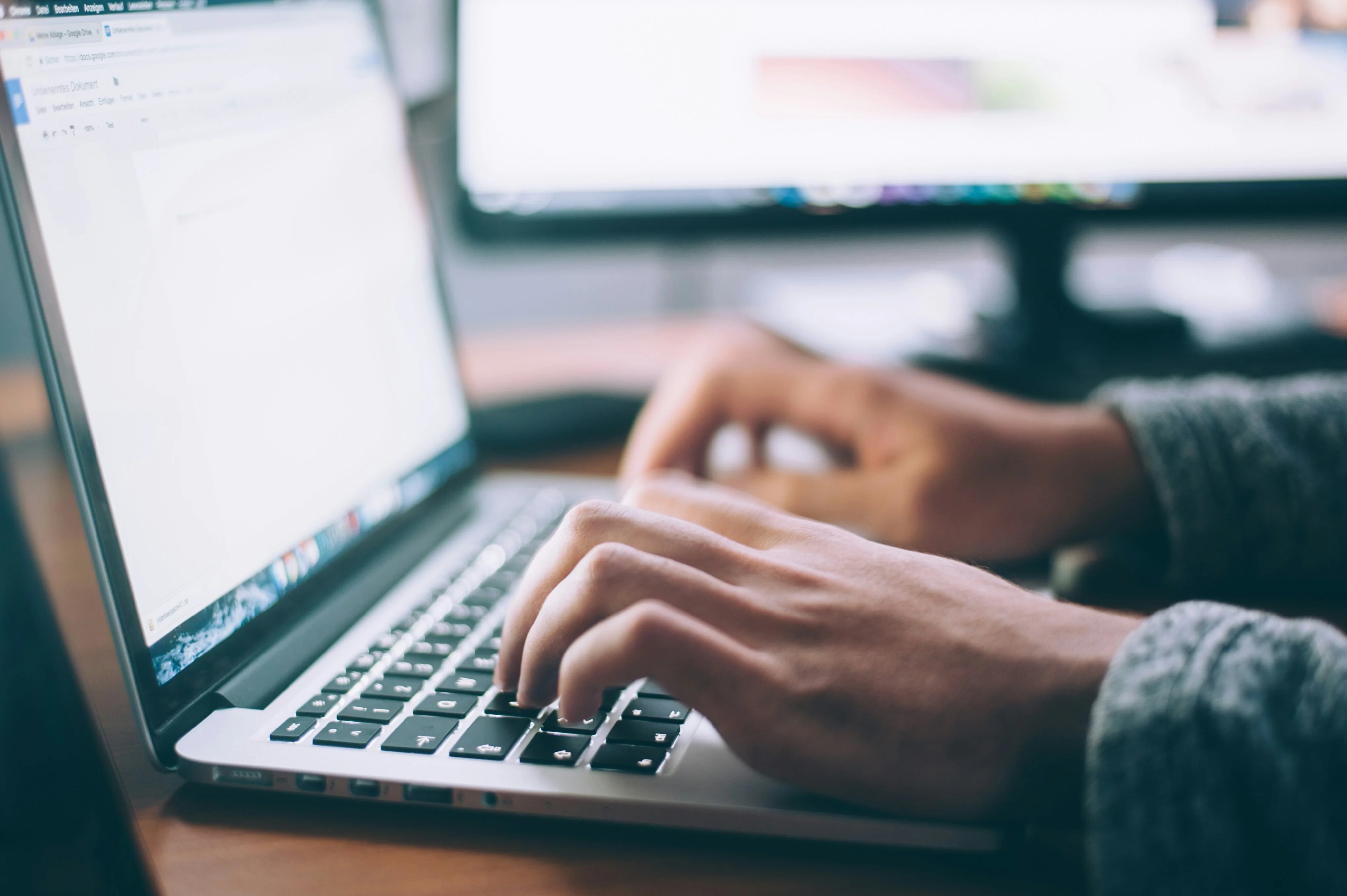 Mains tapant sur le clavier d’un ordinateur portable, avec un second écran derrière
