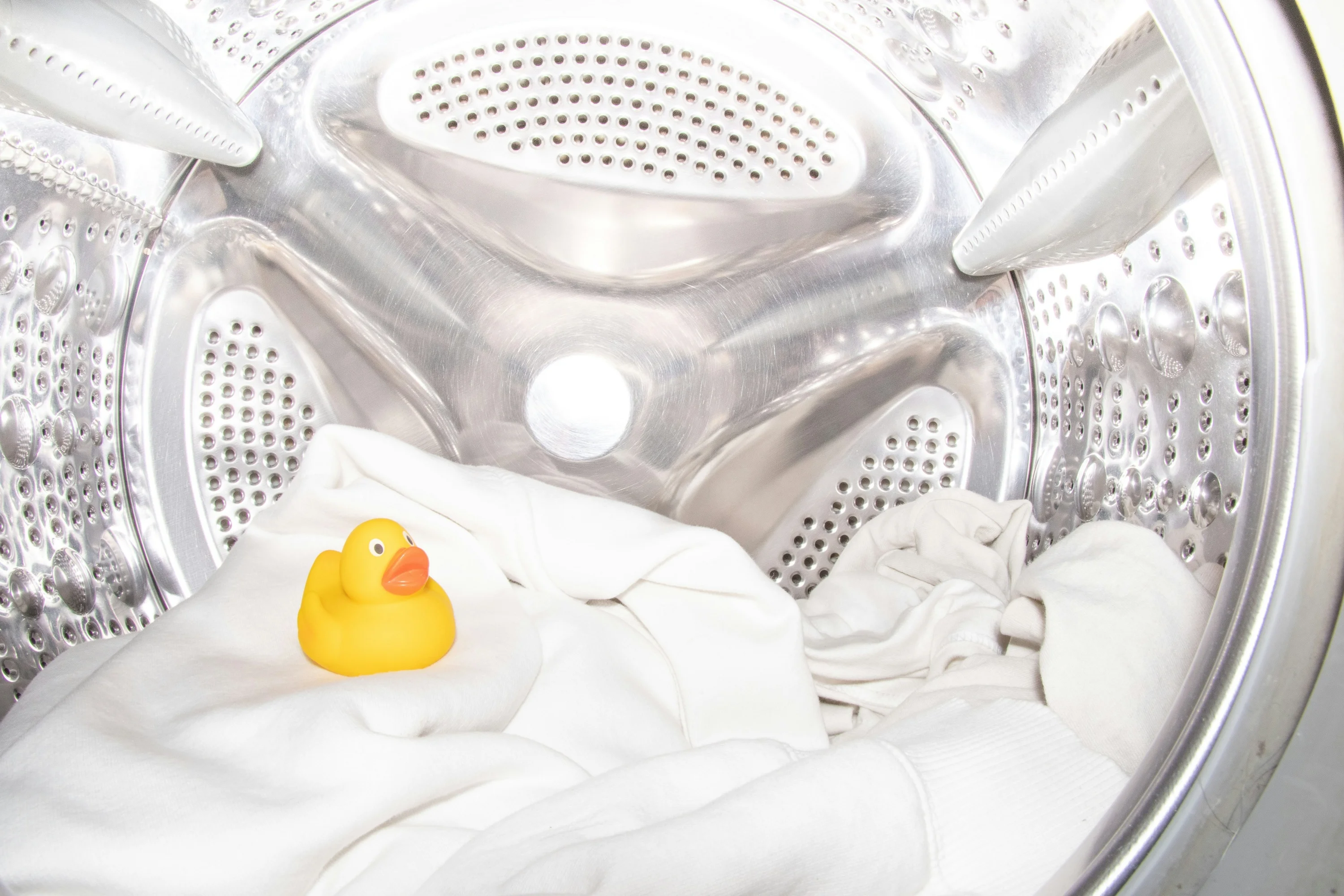 Canard en plastique posé sur du linge blanc dans le tambour d’un lave-linge