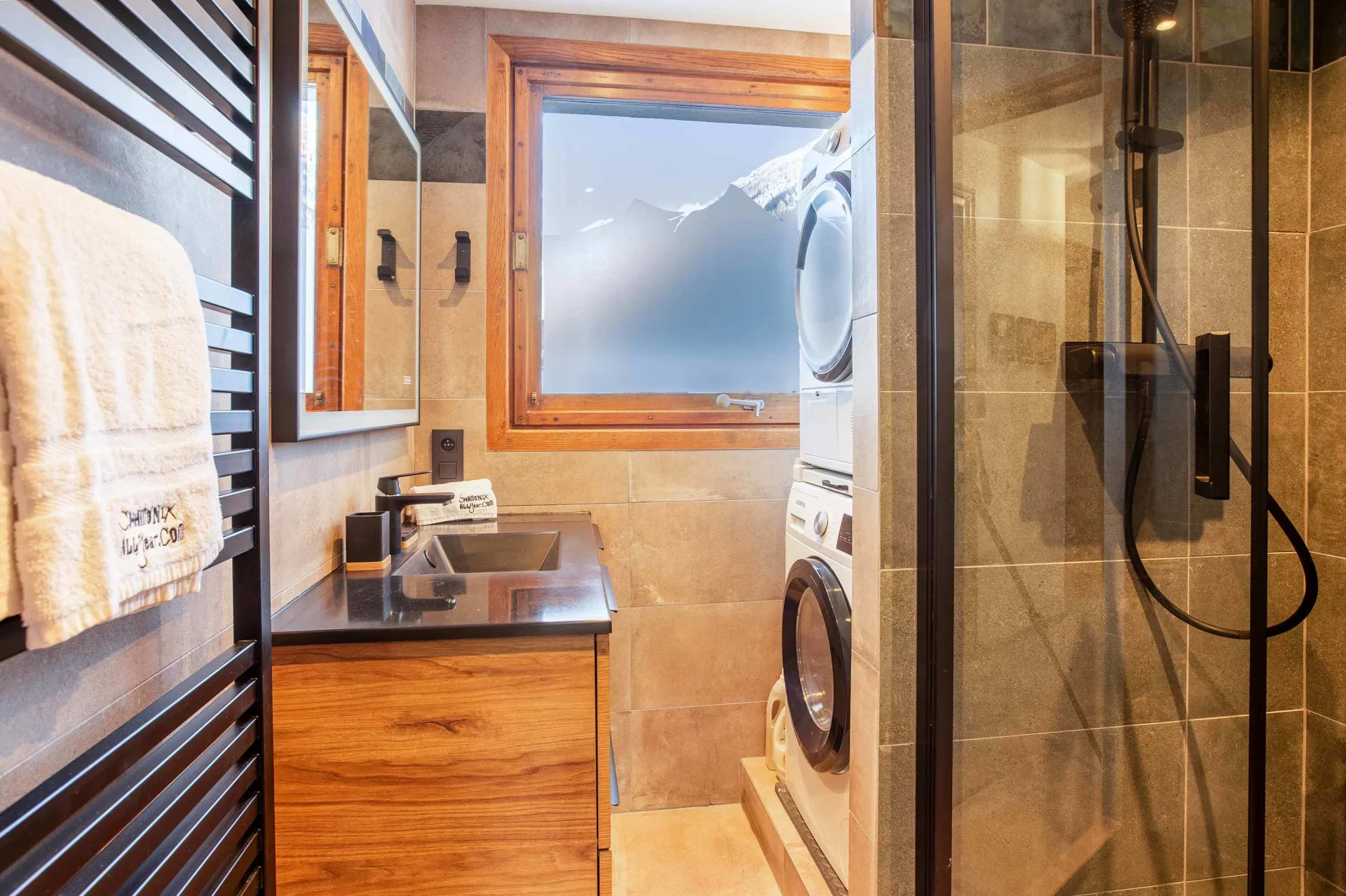 Salle d’eau dans un chalet à Chamonix avec lave-linge et sèche-linge superposés et fenêtre donnant sur les montagnes