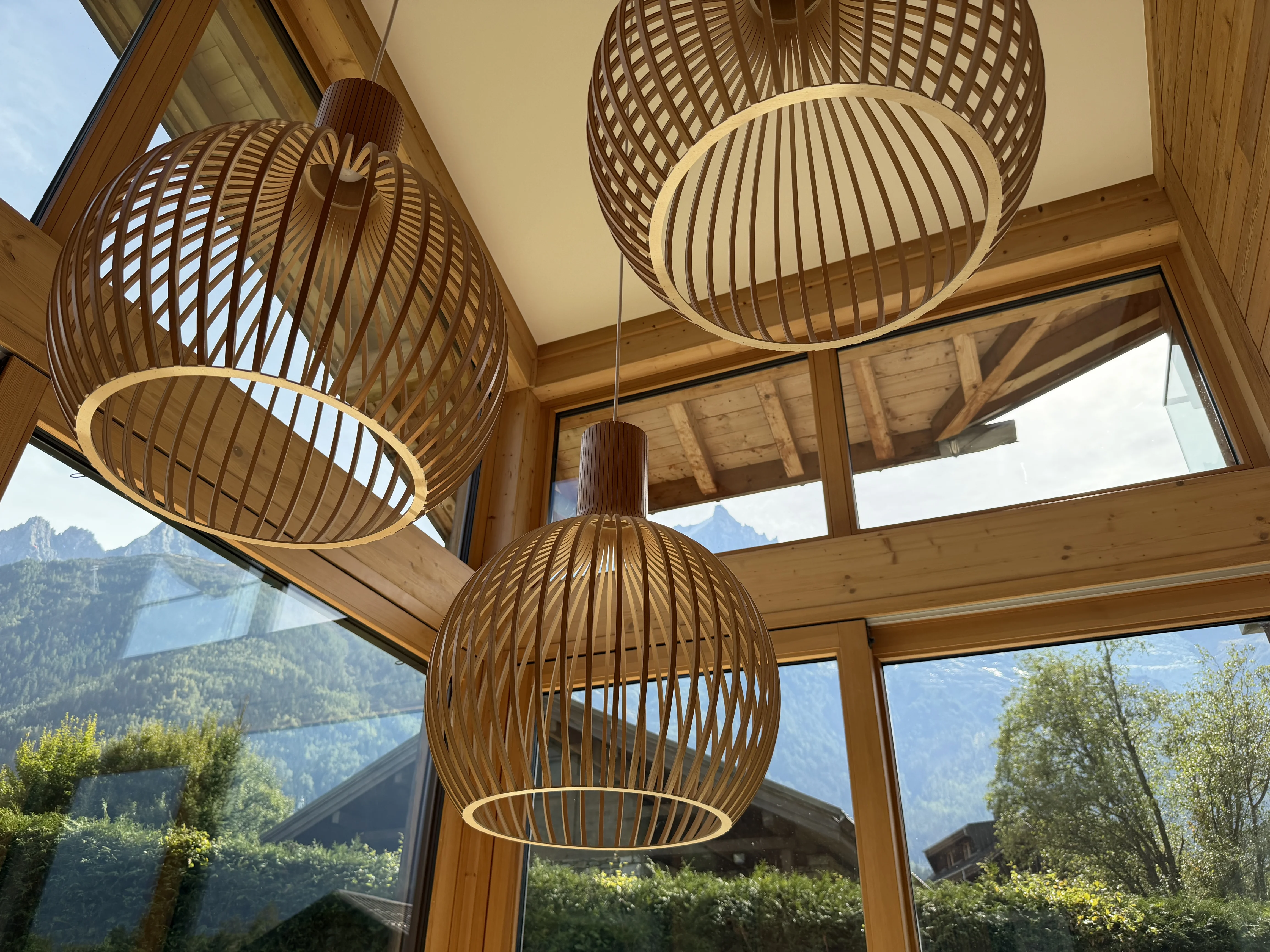 Woven pendant lights hanging in front of floor to ceiling chalet windows in Chamonix, with the Aiguilles beyond