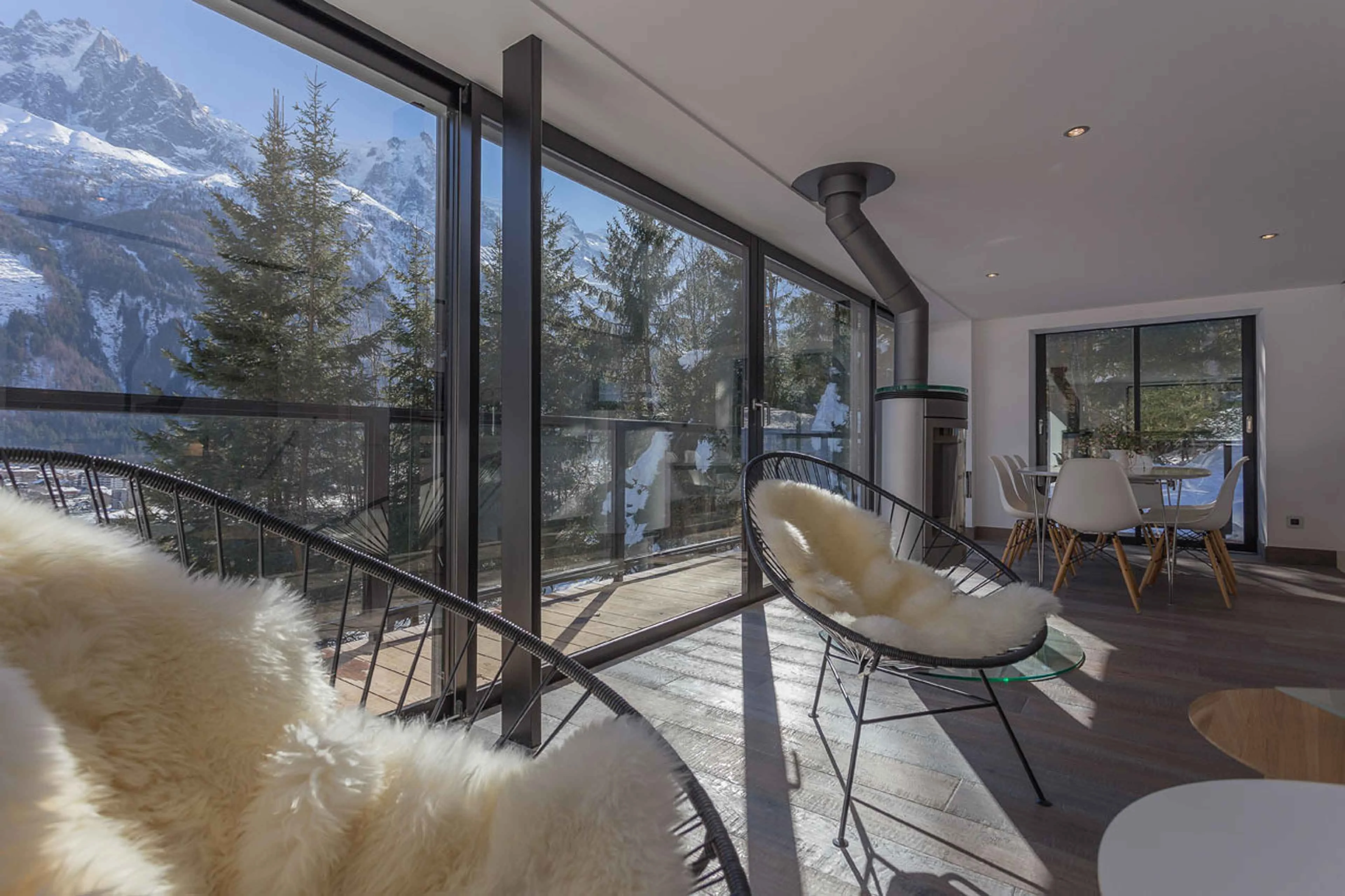 Living room in a Chamonix apartment with sheepskin chairs, a wood burner and glass doors onto a snowy balcony