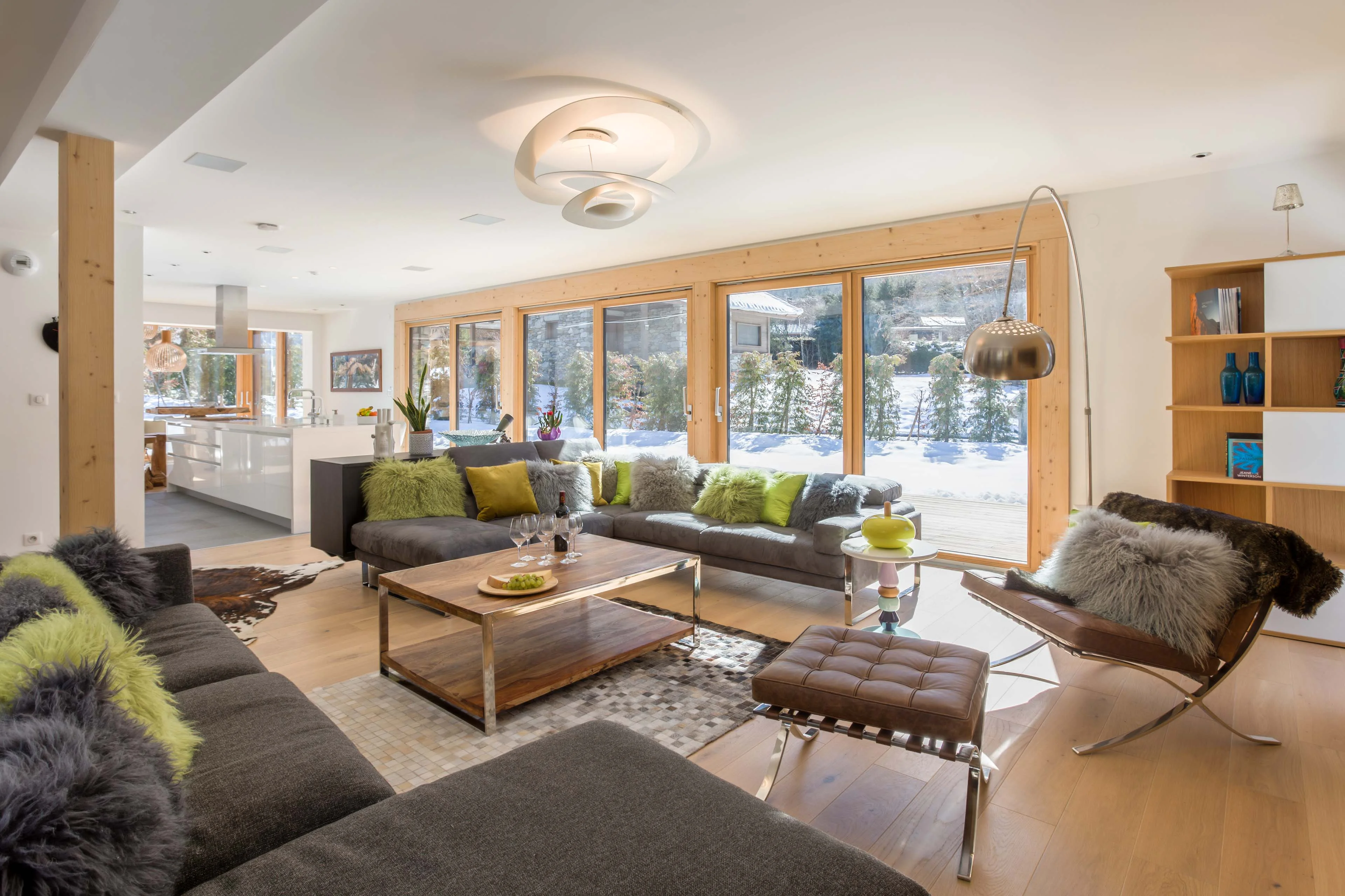 Open plan chalet living room in Chamonix with two large sofas, an open kitchen and windows onto the snowy garden