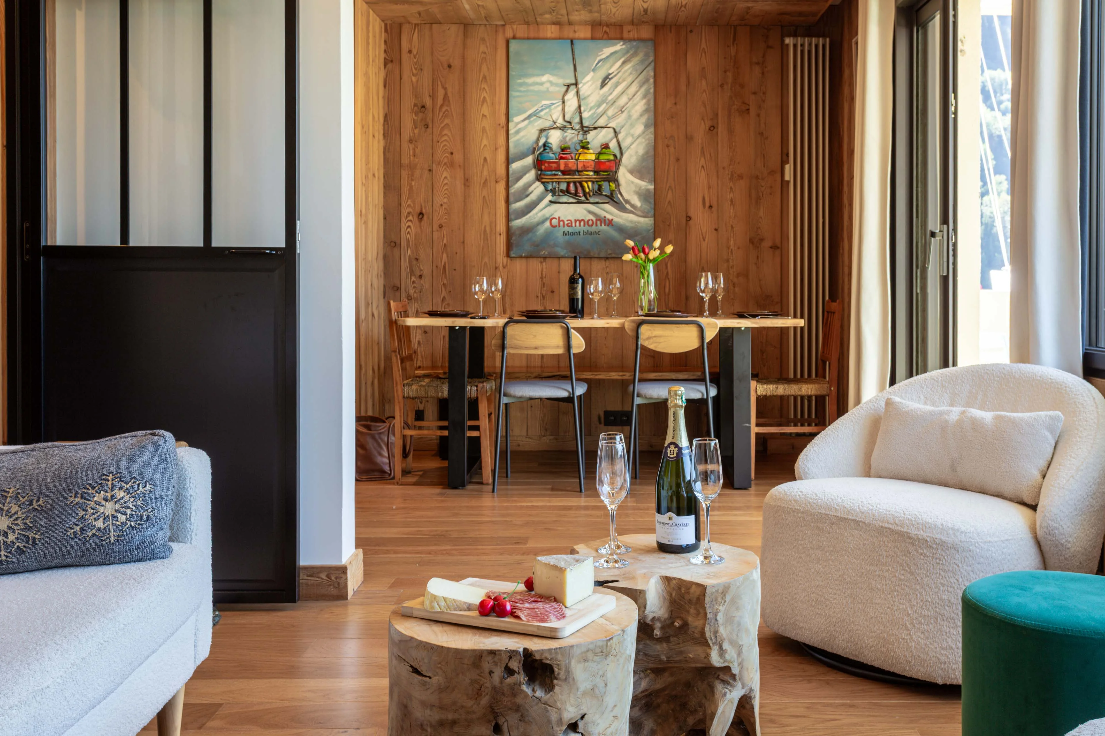 Living and dining area in a Chamonix apartment with timber panelling, a cheese board and a dining table for four