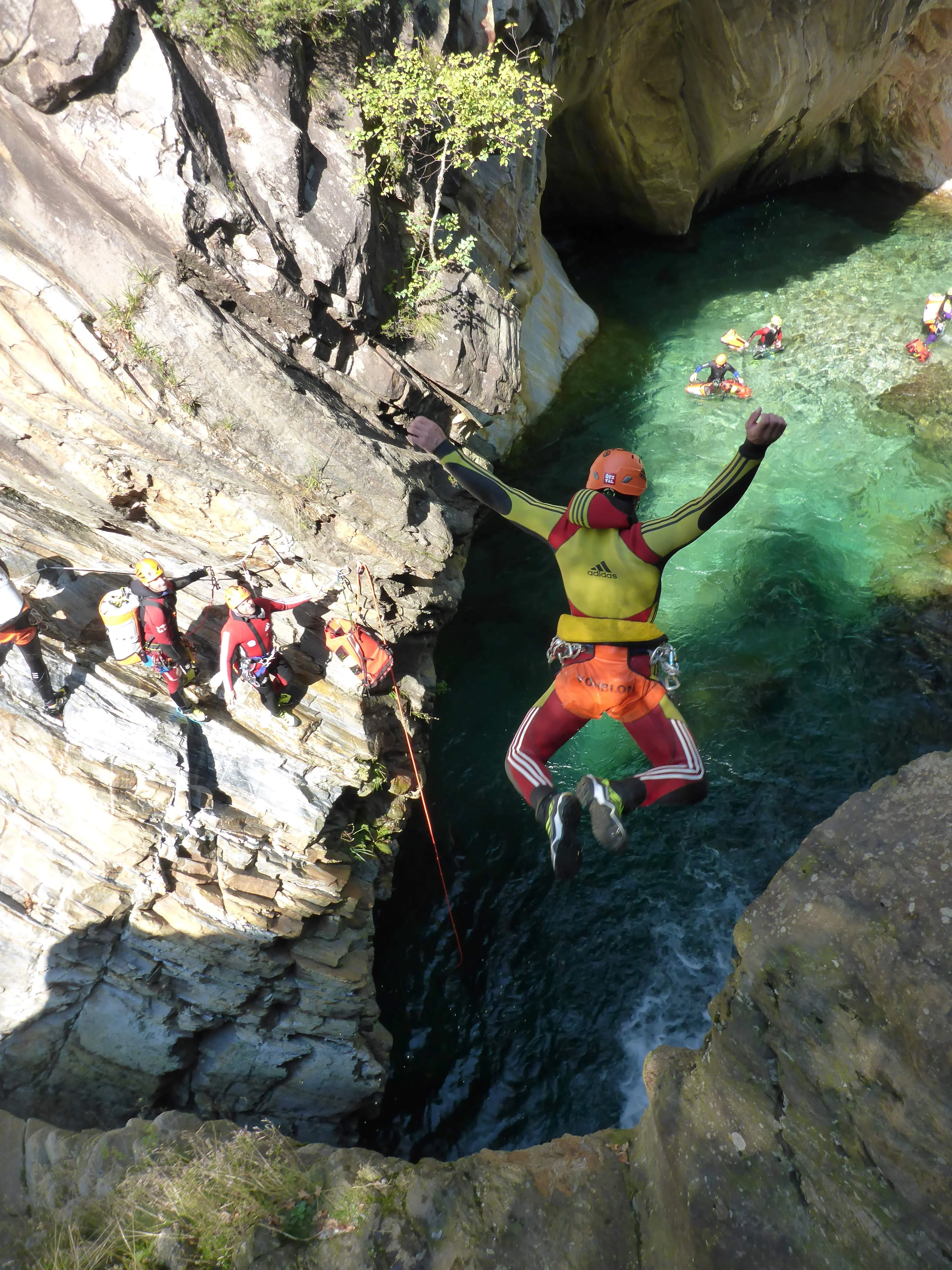 Woman leaping from a rock in a wetsuit and harness with a helmet, into a blue lagoon in the mountains 